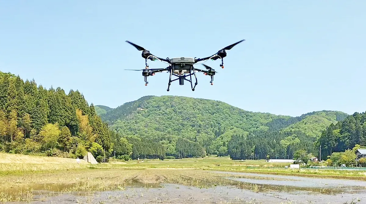 山あいの水田上空を飛行する散布ドローン