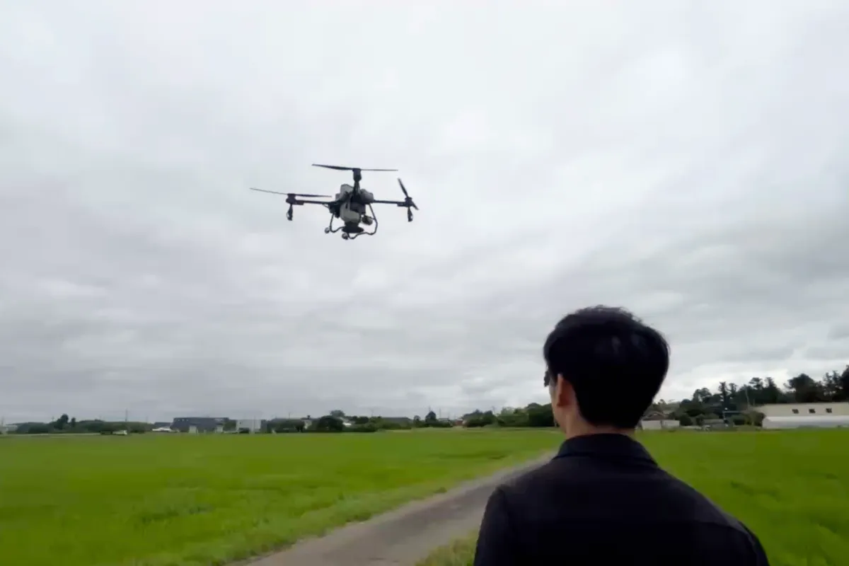 水田の上を飛行する農業用ドローンとそれを見守るオペレーター